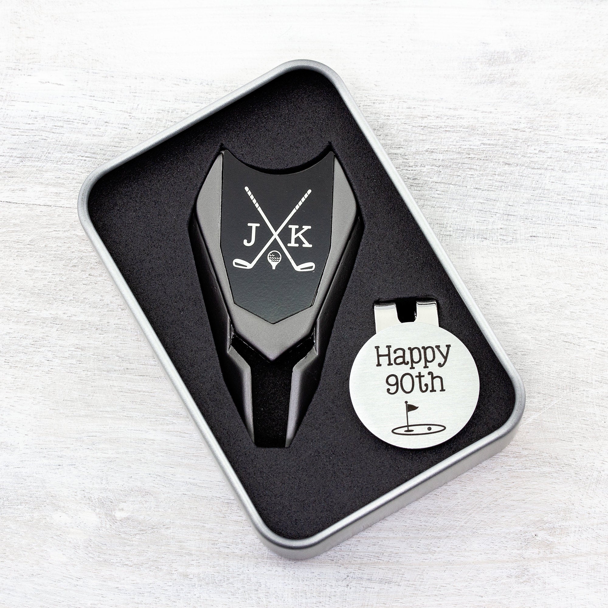 Golf ball marker and divot tool gift tin set personalized. Divot tool has crossed clubs with initials on each side. Round ball marker with hat clip has happy 90th  with golf flag graphic engraved.