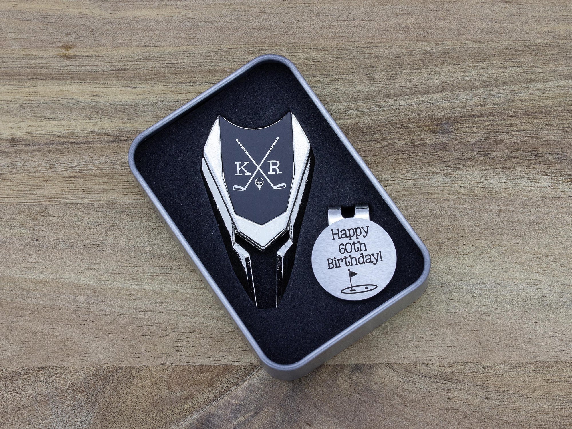 Golf ball marker and divot tool gift tin set personalized. Divot tool has crossed clubs with initials on each side. Round ball marker with hat clip has happy 60th birthday with golf flag graphic engraved.