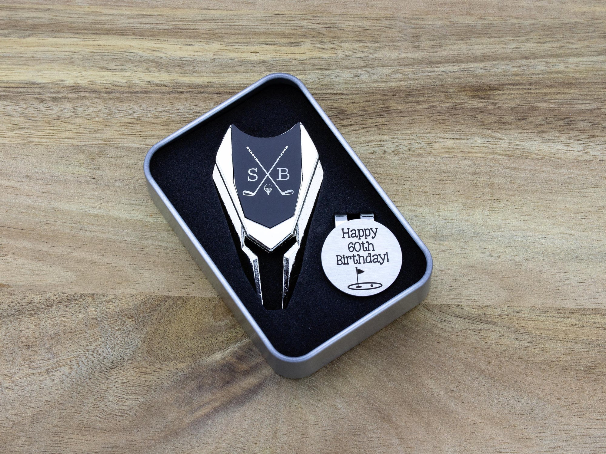 Golf ball marker and divot tool gift tin set personalized. Divot tool has crossed clubs with initials on each side. Round ball marker with hat clip has happy 60th birthday with golf flag graphic engraved.
