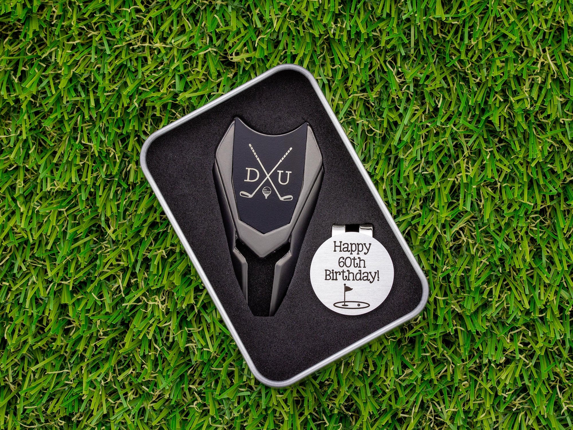 Golf ball marker and divot tool gift tin set personalized. Divot tool has crossed clubs with initials on each side. Round ball marker with hat clip has happy 60th birthday with golf flag graphic engraved.