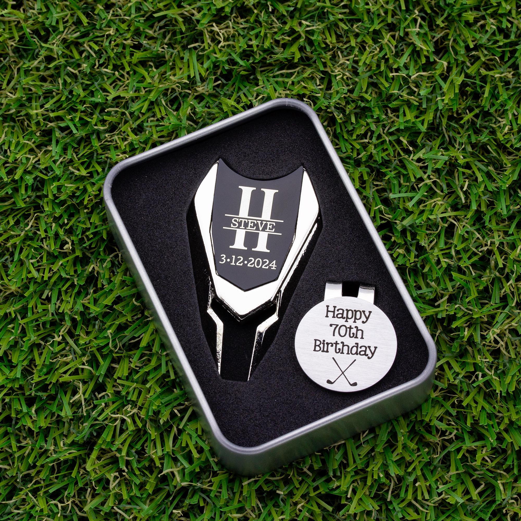 Golf ball marker and divot tool gift tin set personalized. Divot tool has crossed clubs with initials on each side. Round ball marker with hat clip has happy 70th birthday with golf flag graphic engraved.