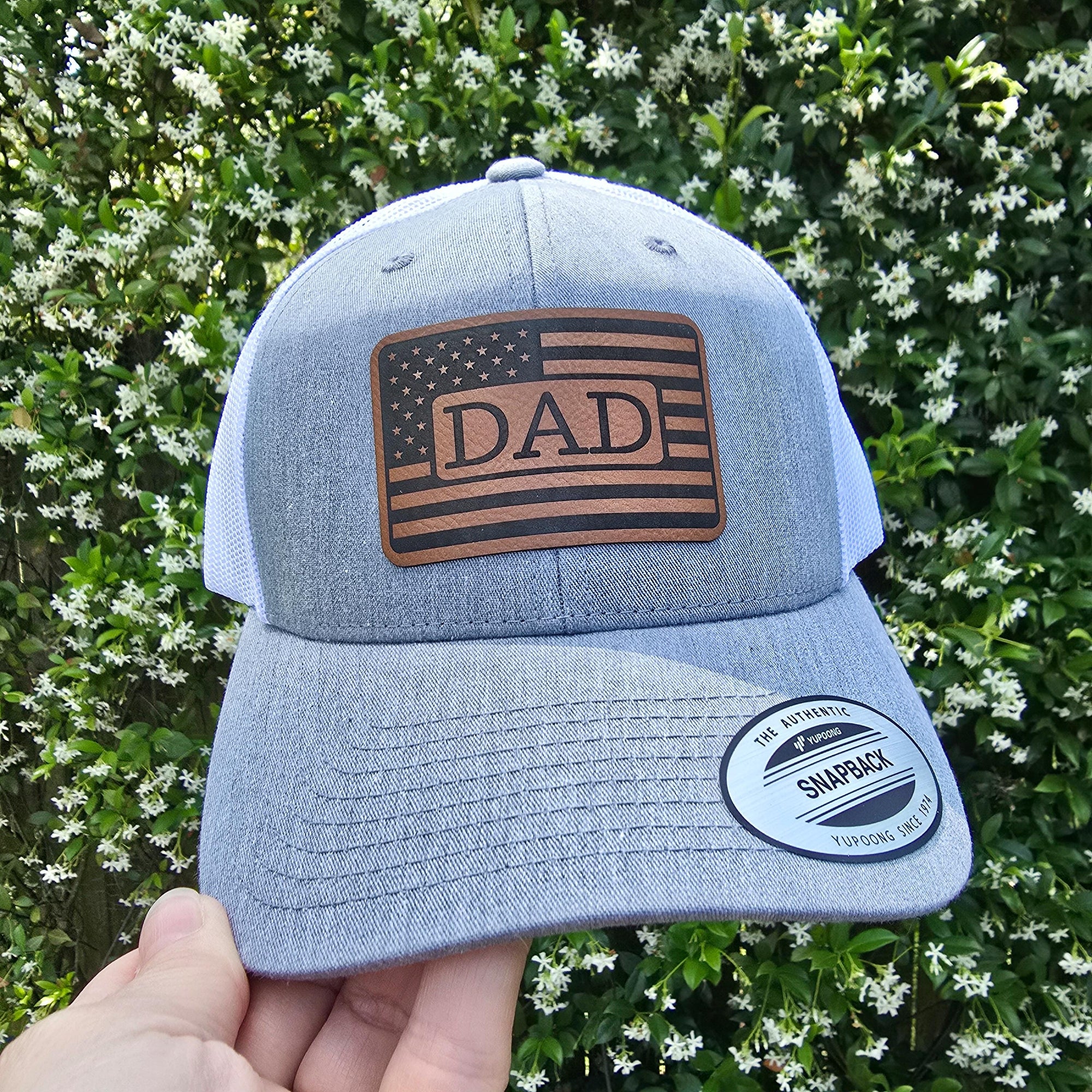 heather and white snapback trucker hat with brown leather patch engraved with  american flag and DAD in center.