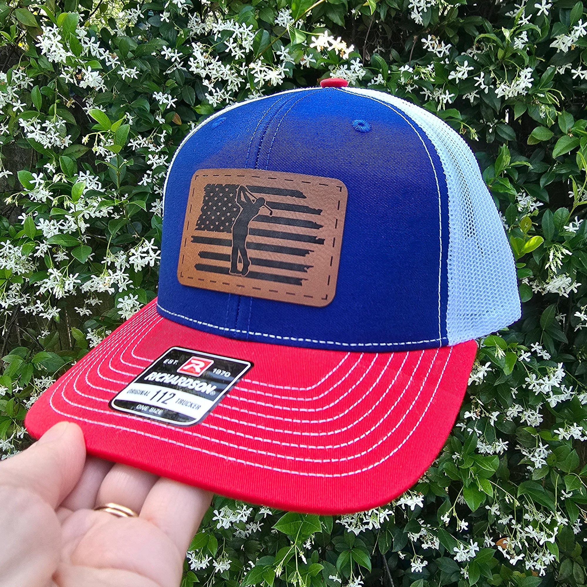 red blue and white snapback trucker hat with brown leather patch engraved with golfer swinging over american flag.