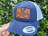 navy and white snapback trucker hat with leather patch engraved with large crossing fish hooks and Grandpa in center.